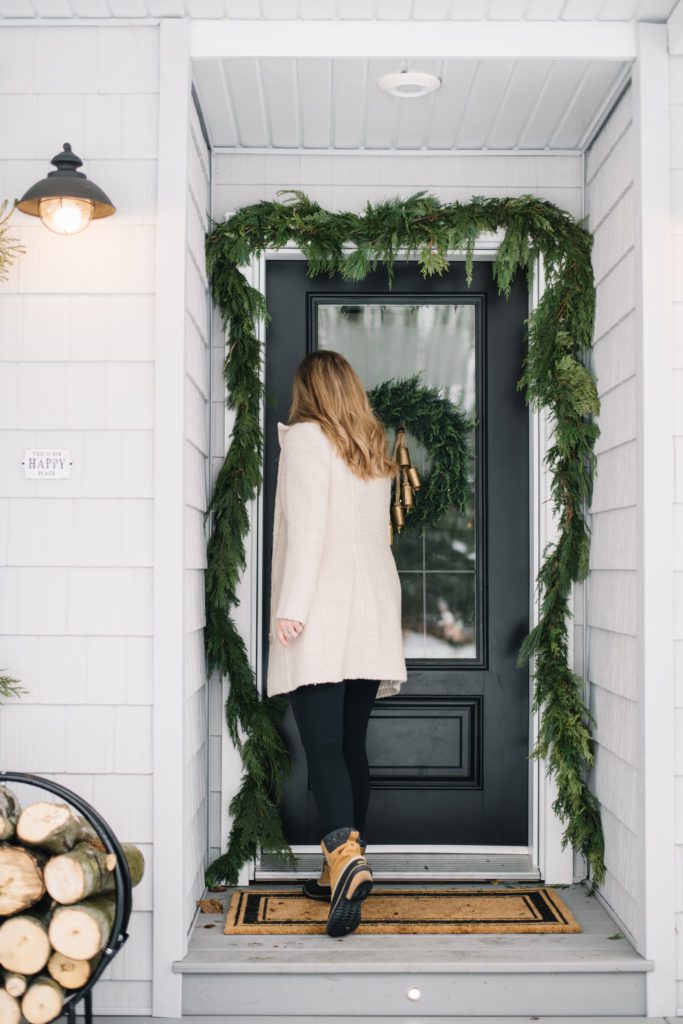 A woman walking into a front door decorated for Christmas