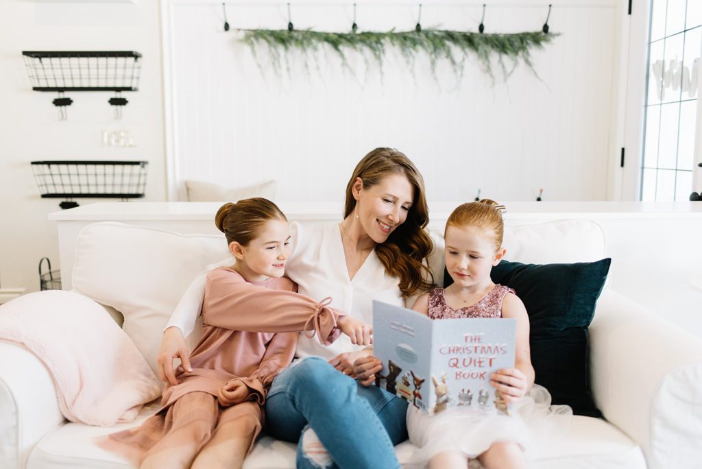 A woman sitting on a couch reading a book to her daughters