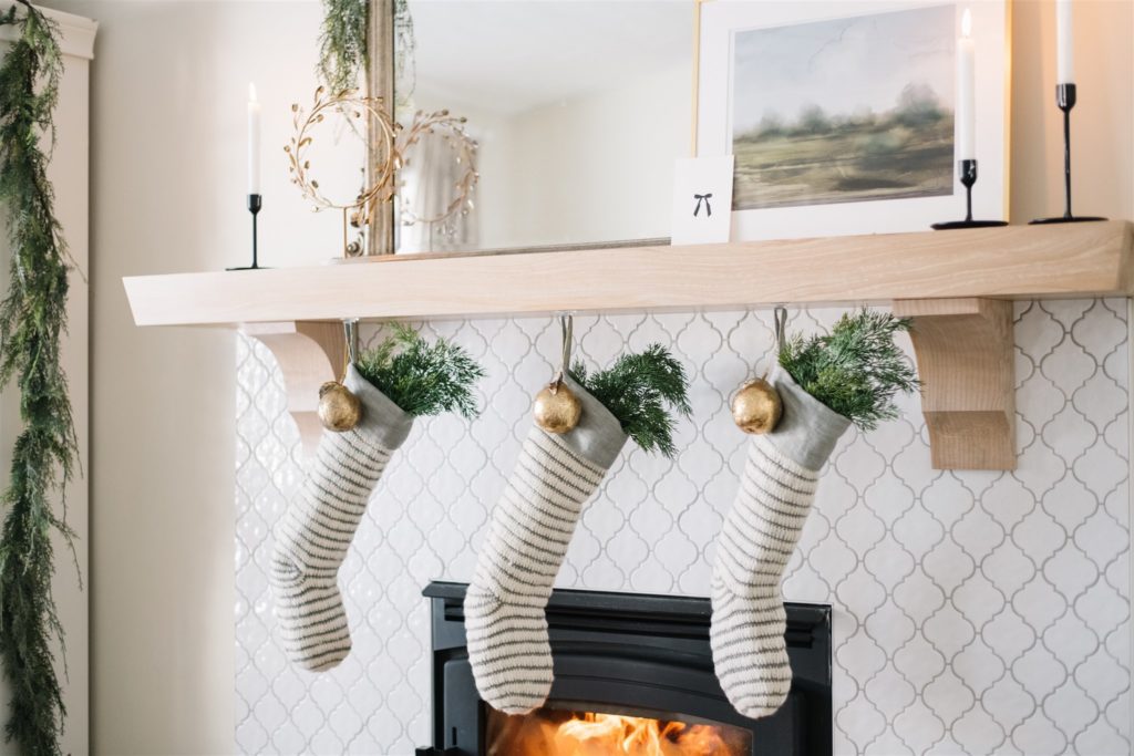 grey stiped stocking stuffed with greens hang on neutral christmas mantle