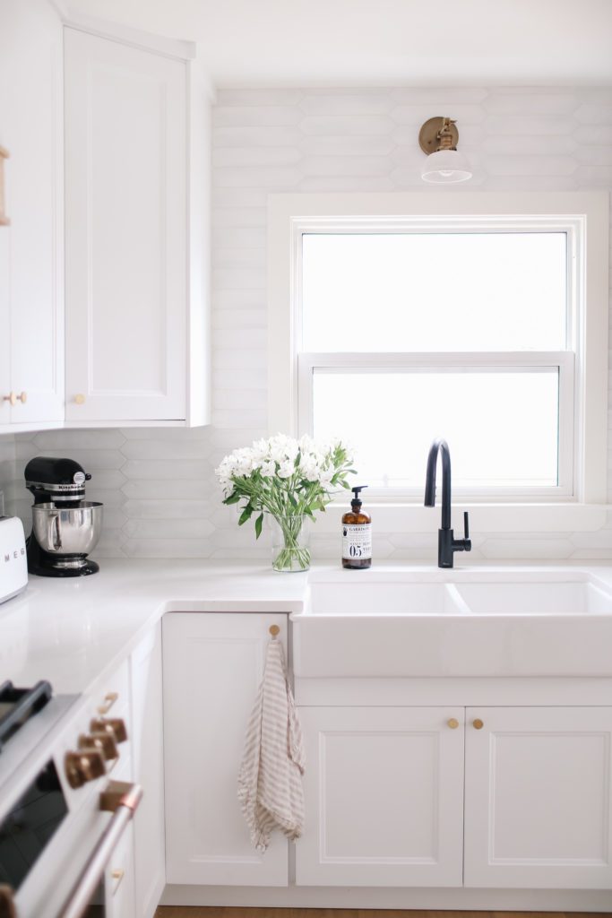 A white kitchen with a farmhouse sink and a black faucet with fresh flowers sitting beside
