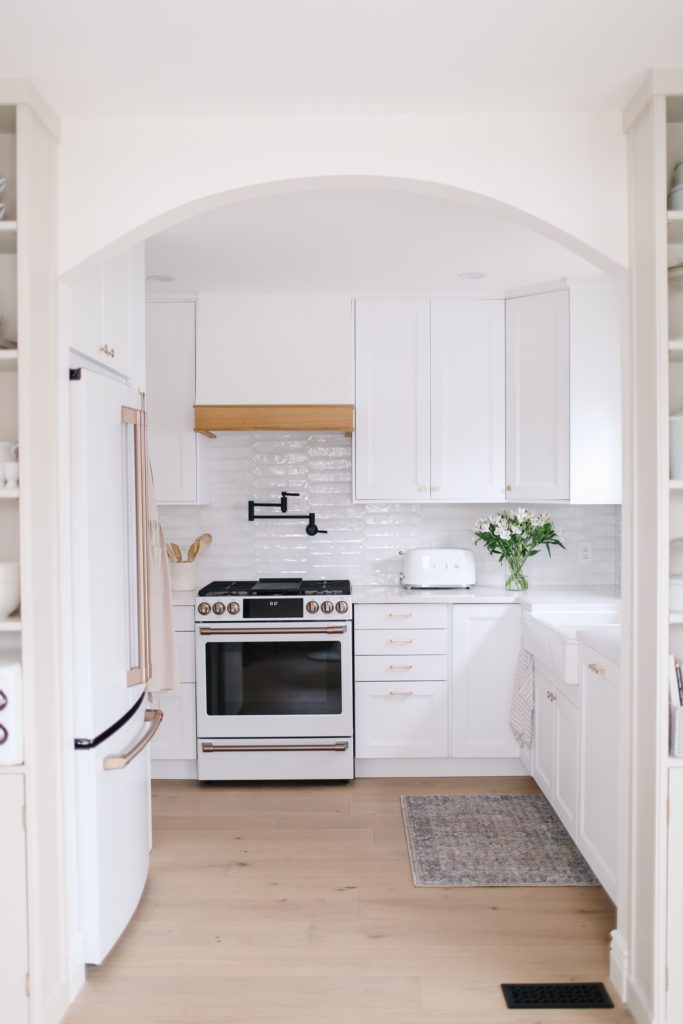 An arched opening into a small white kitchen