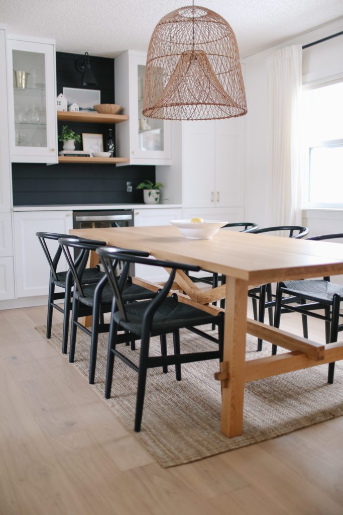 A white oak dining room table with black chairs and an oversize pendant