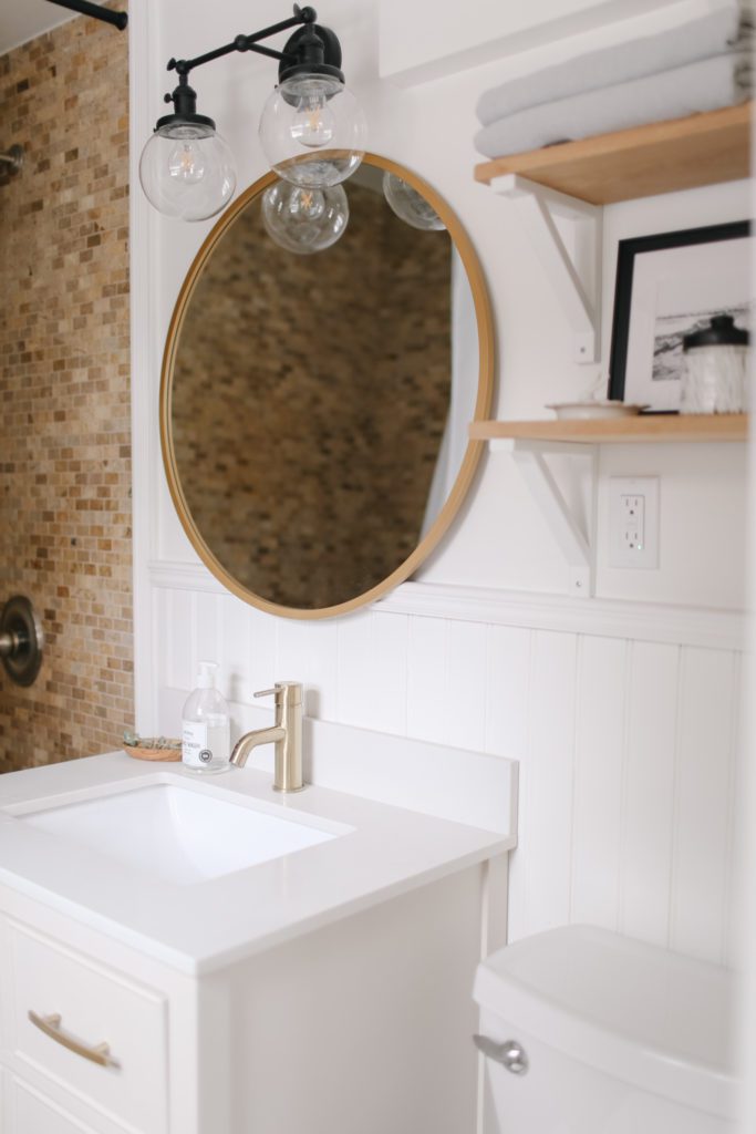 A white bathroom sink and round gold framed mirror